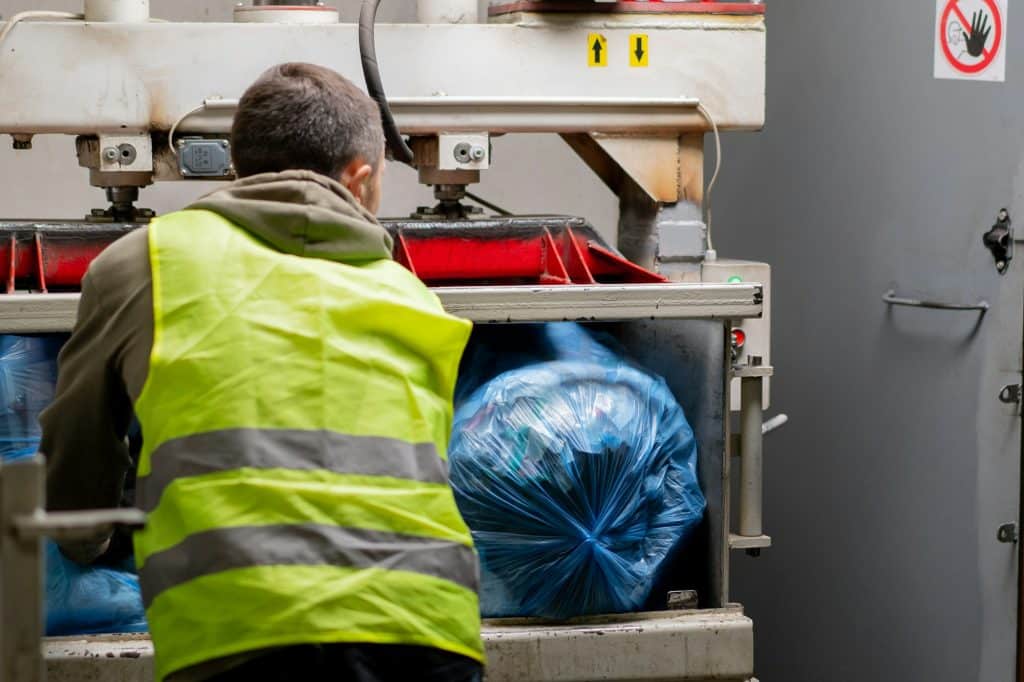 Trusted Best Sump Pump, Water Heater, and Garbage Disposal Service & Repair in Northeast Indiana | A recycling plant employee in uniform puts bags of garbage into special press machine waste disposal