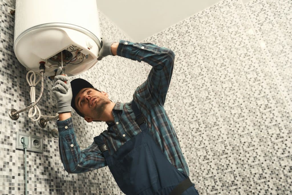 Trusted Emergency Plumber, Plumbing Emergency, Drain Unclogging, Water Line Repair in Northeast Indiana | Plumber installing electric heating boiler. Young handyman in uniform setting up electric heating